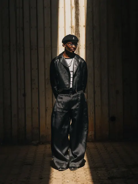 A person in wide-leg trousers and a leather jacket standing in sunlight.