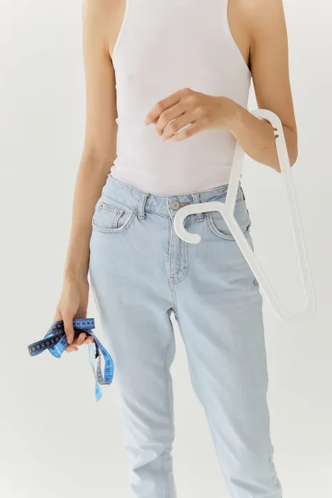 A woman wearing jeans holding a clothes hanger and measuring tape.