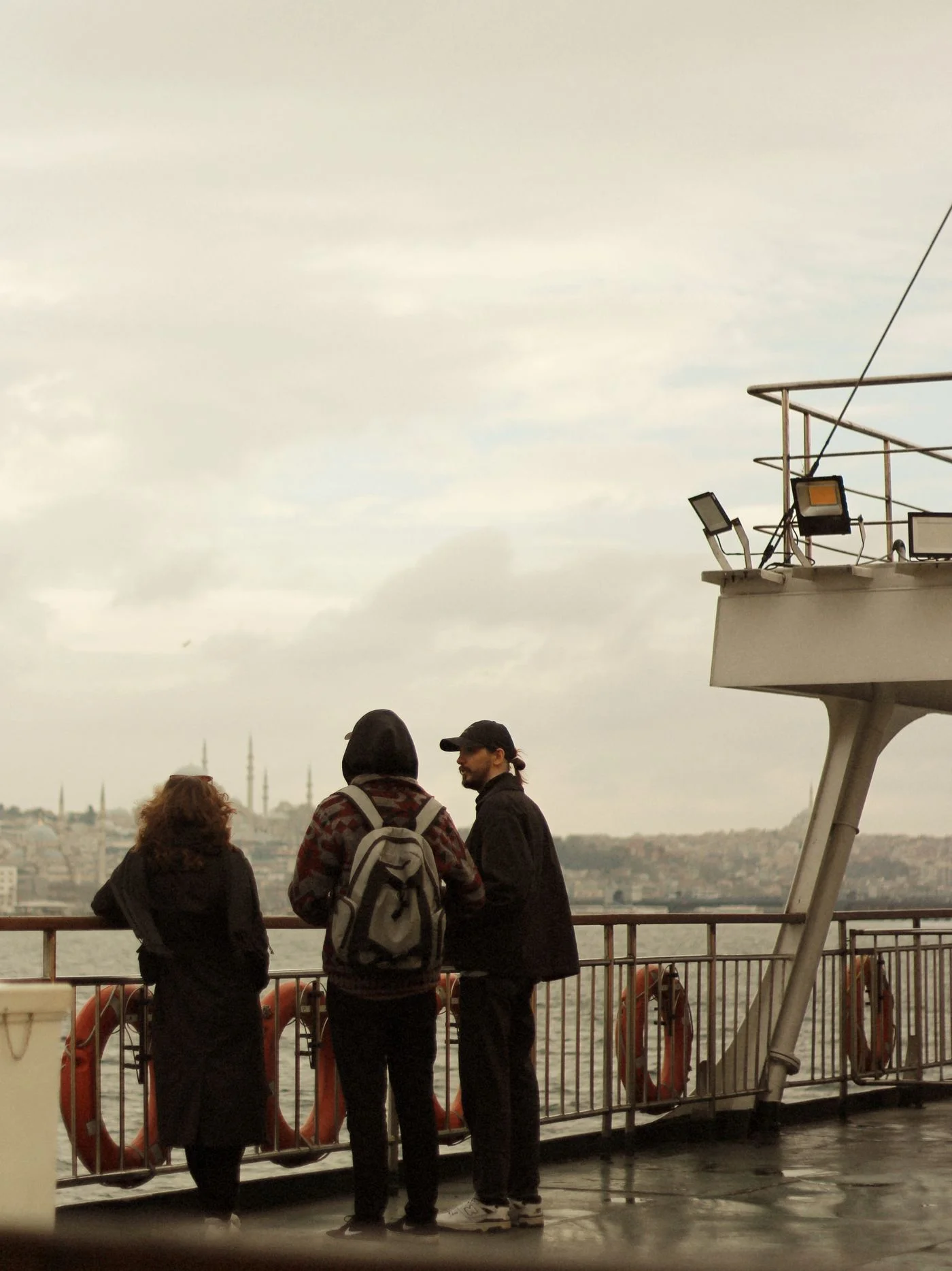 Three people standing on a ferry deck and looking across the water.