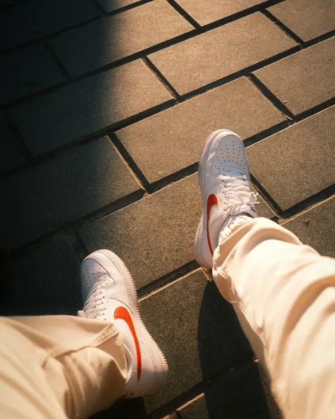 Pale sneakers with red accents worn on sunlit pavement.
