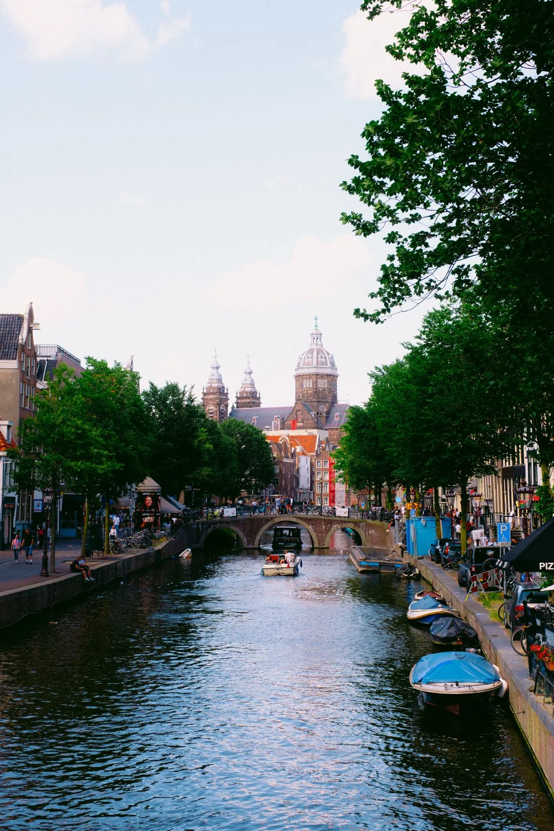 Amsterdam canal with boats, trees, a stone bridge and distant domes