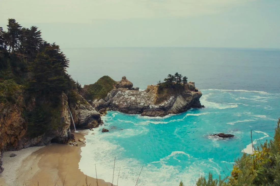 A rocky coastal cove with turquoise water and trees above it