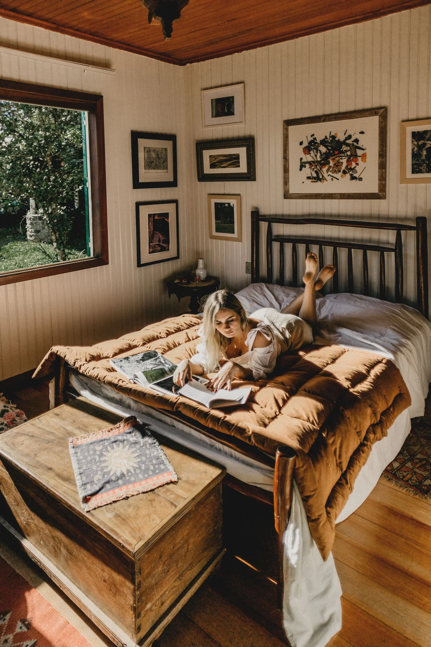 Woman reading while lying on a bed in a room with framed pictures