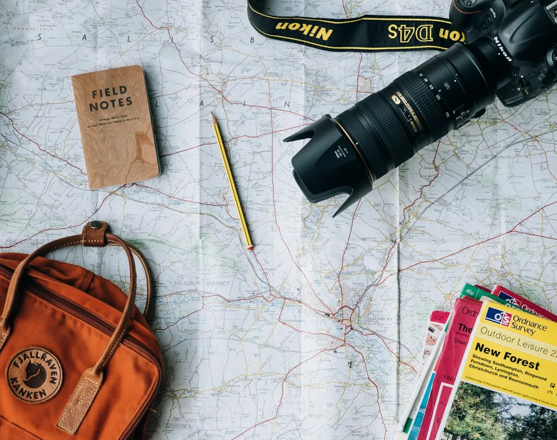 Camera, notebook, pencils and an orange bag arranged on a paper map