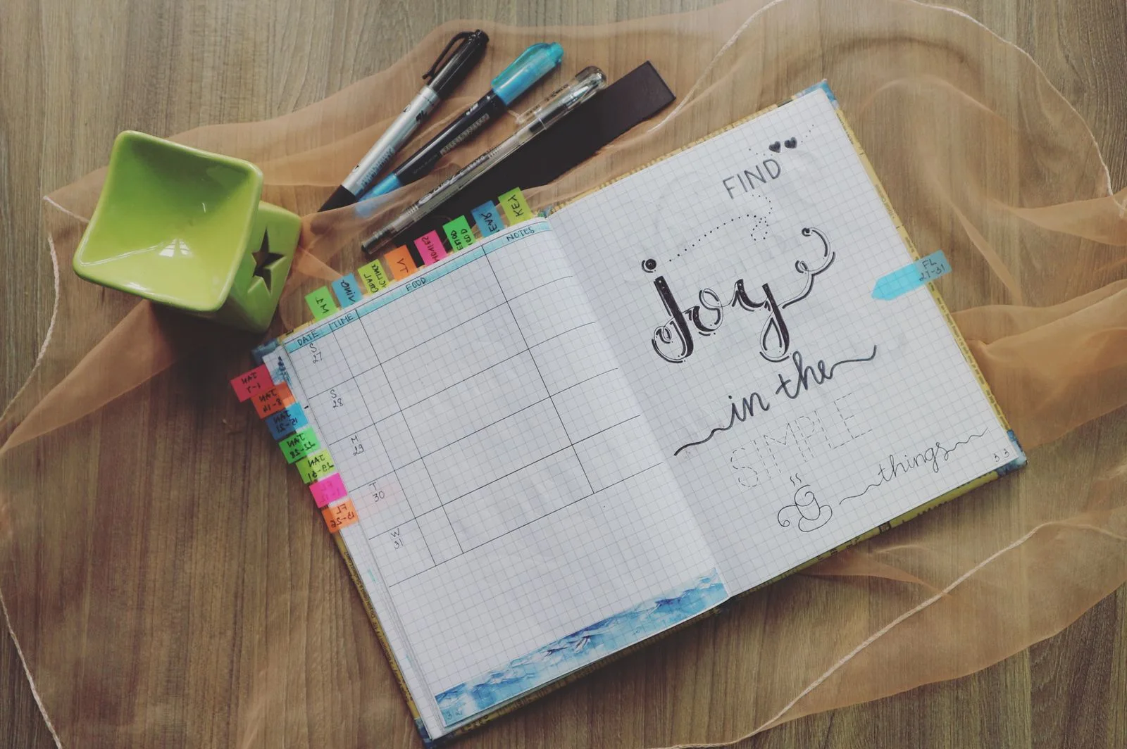 An open planner with colourful tabs and pens on a wooden surface