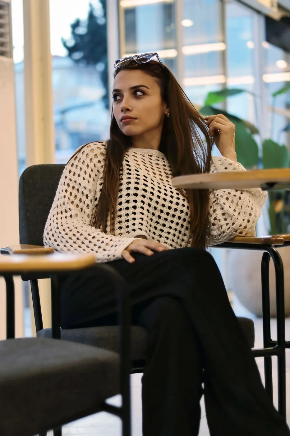 A woman in a patterned top and dark trousers seated at a cafe table.