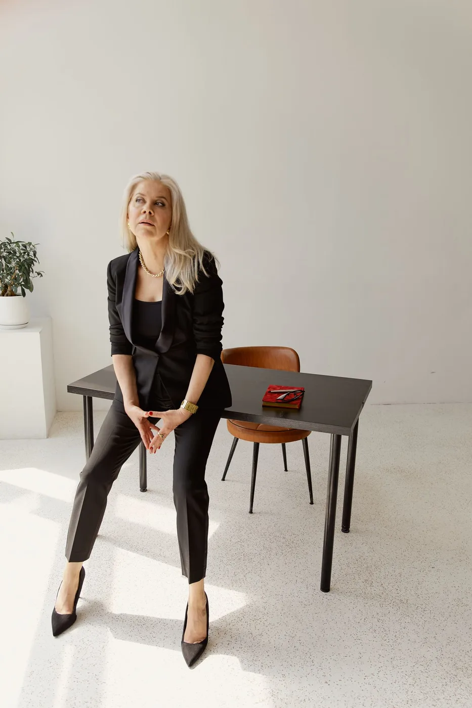 A woman wearing a black blazer and trousers beside a table.