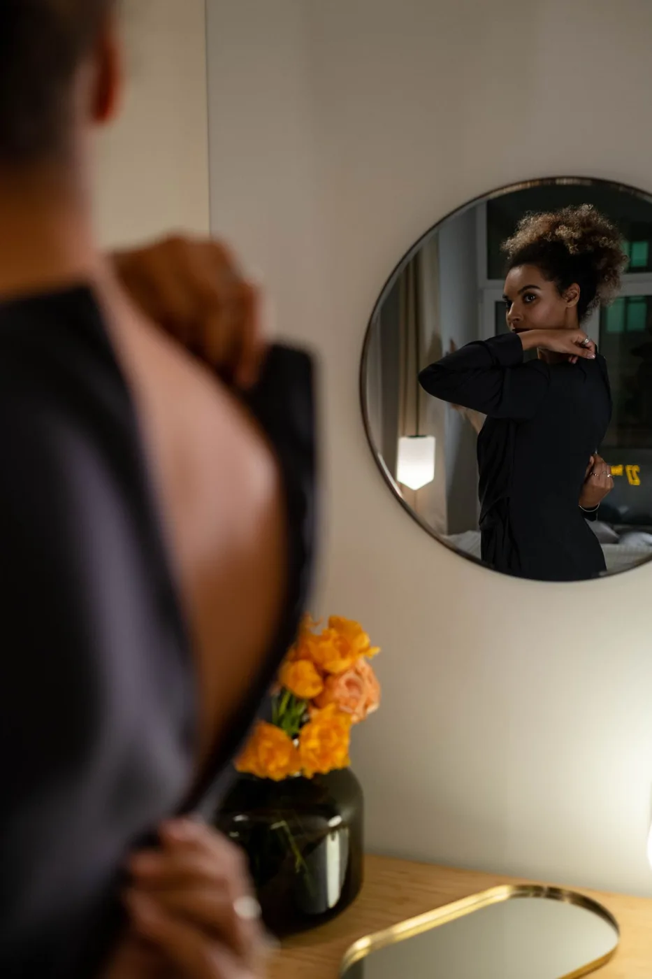 A woman wearing a black dress in front of a round mirror.