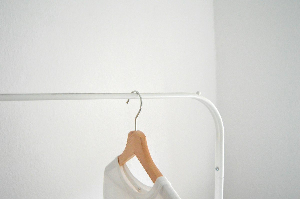 A white shirt hanging from a wooden hanger against a pale wall.