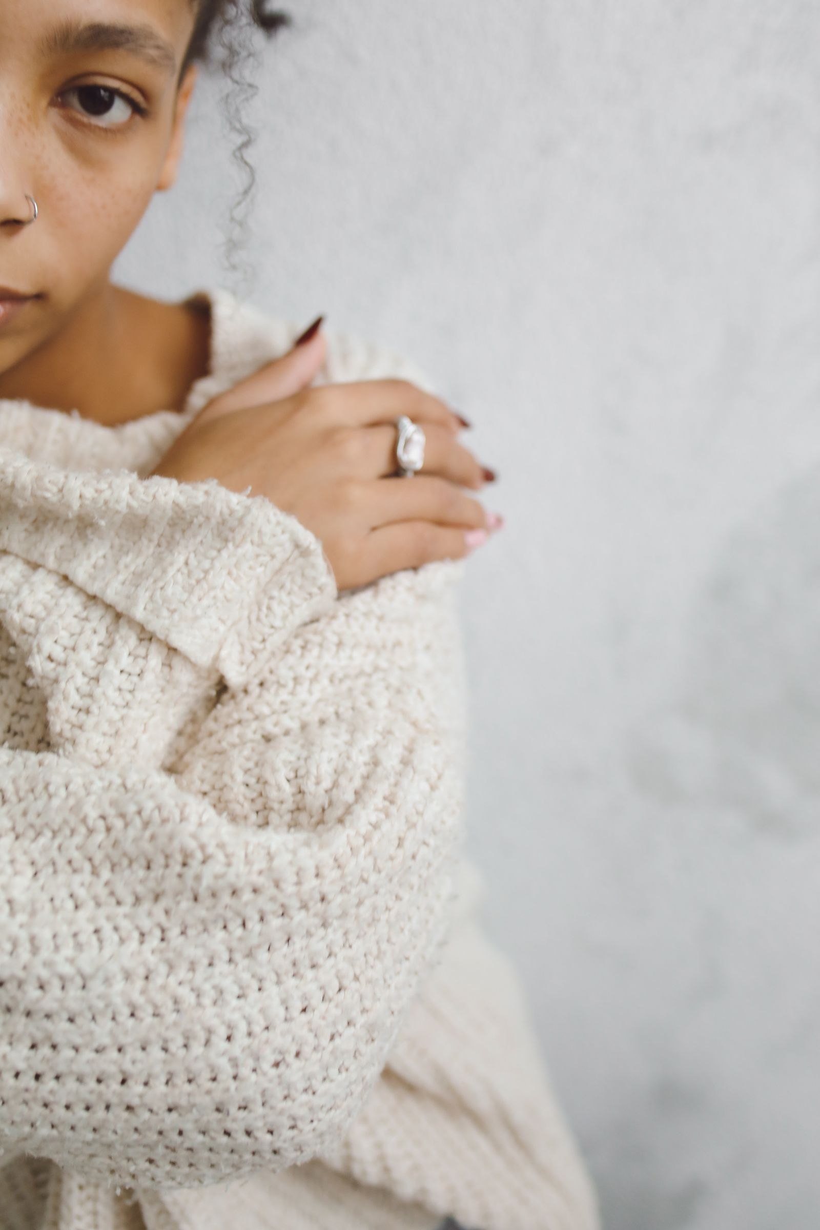 A close view of a cream knitted sleeve beside a hand wearing rings.