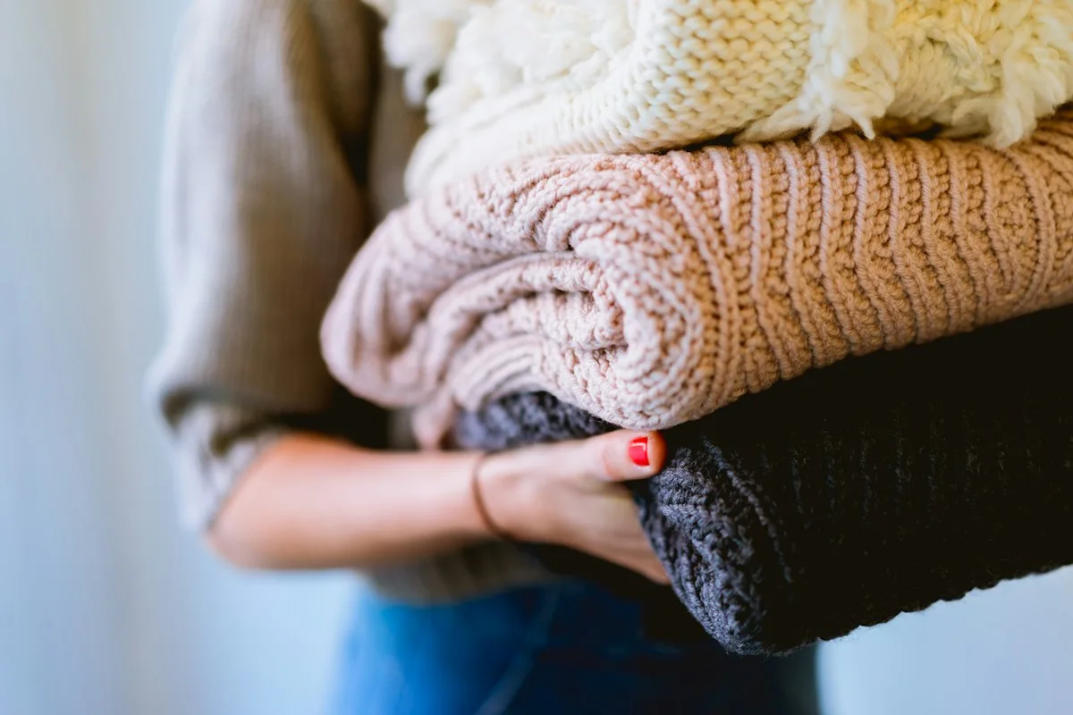 A person carrying a stack of folded knitwear.