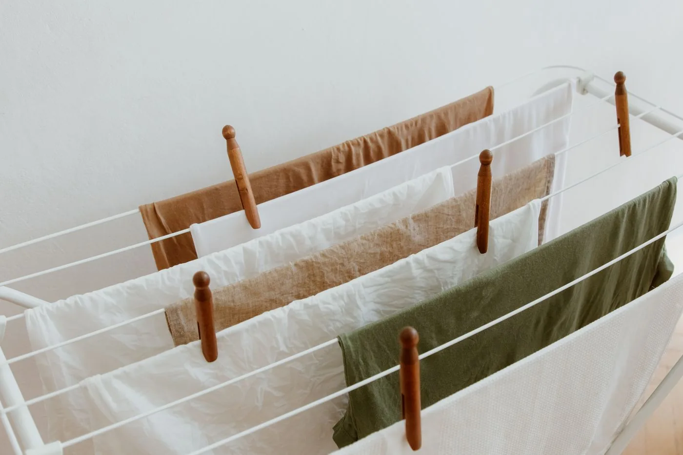 Light-colored laundry hanging on a drying rack with wooden pegs.