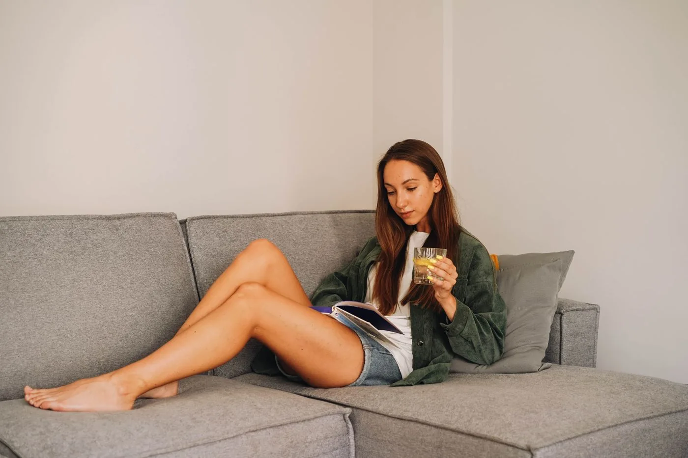 A woman reading a book on a gray sofa.