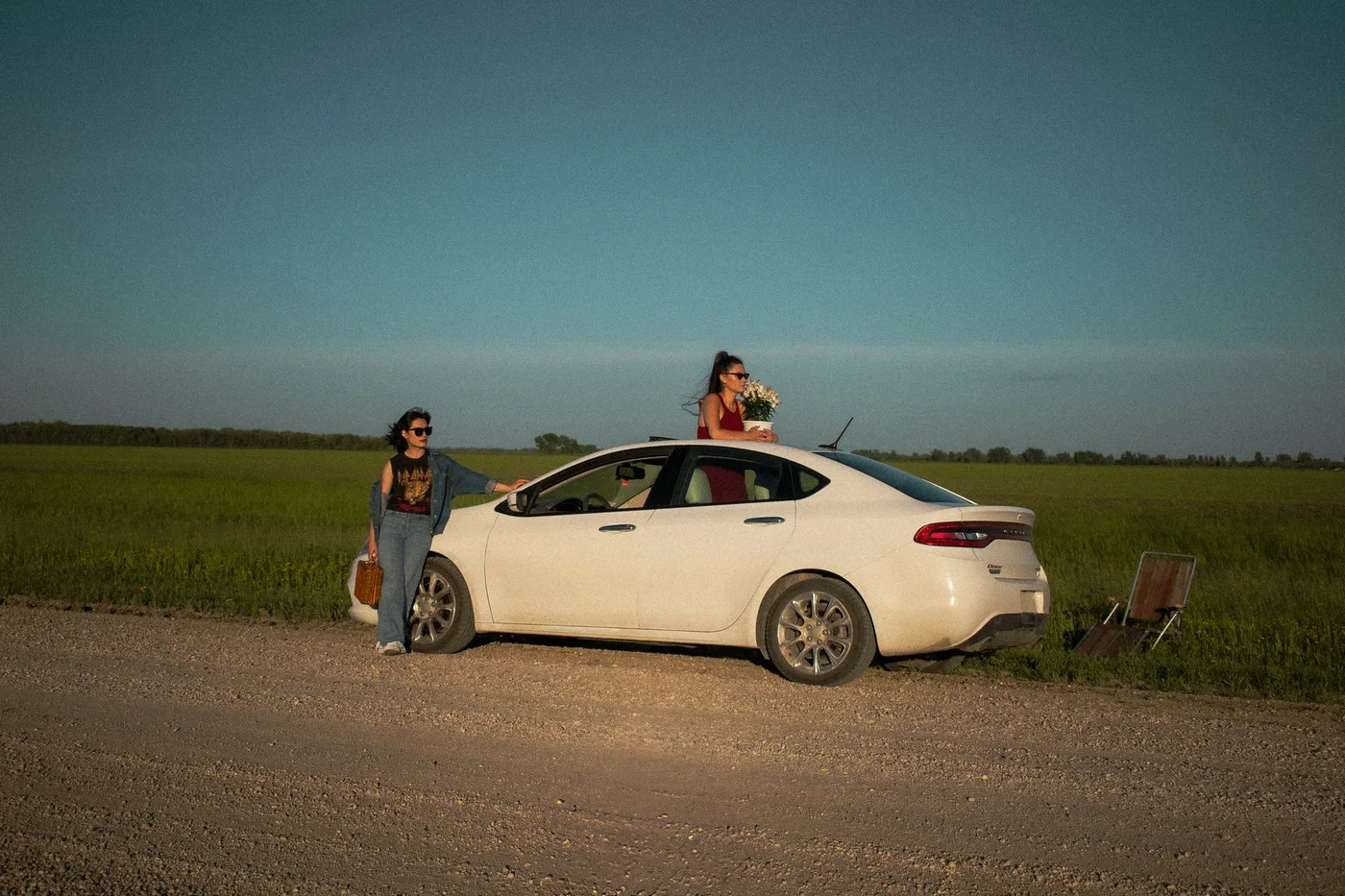 Two women beside a white car in an open landscape.
