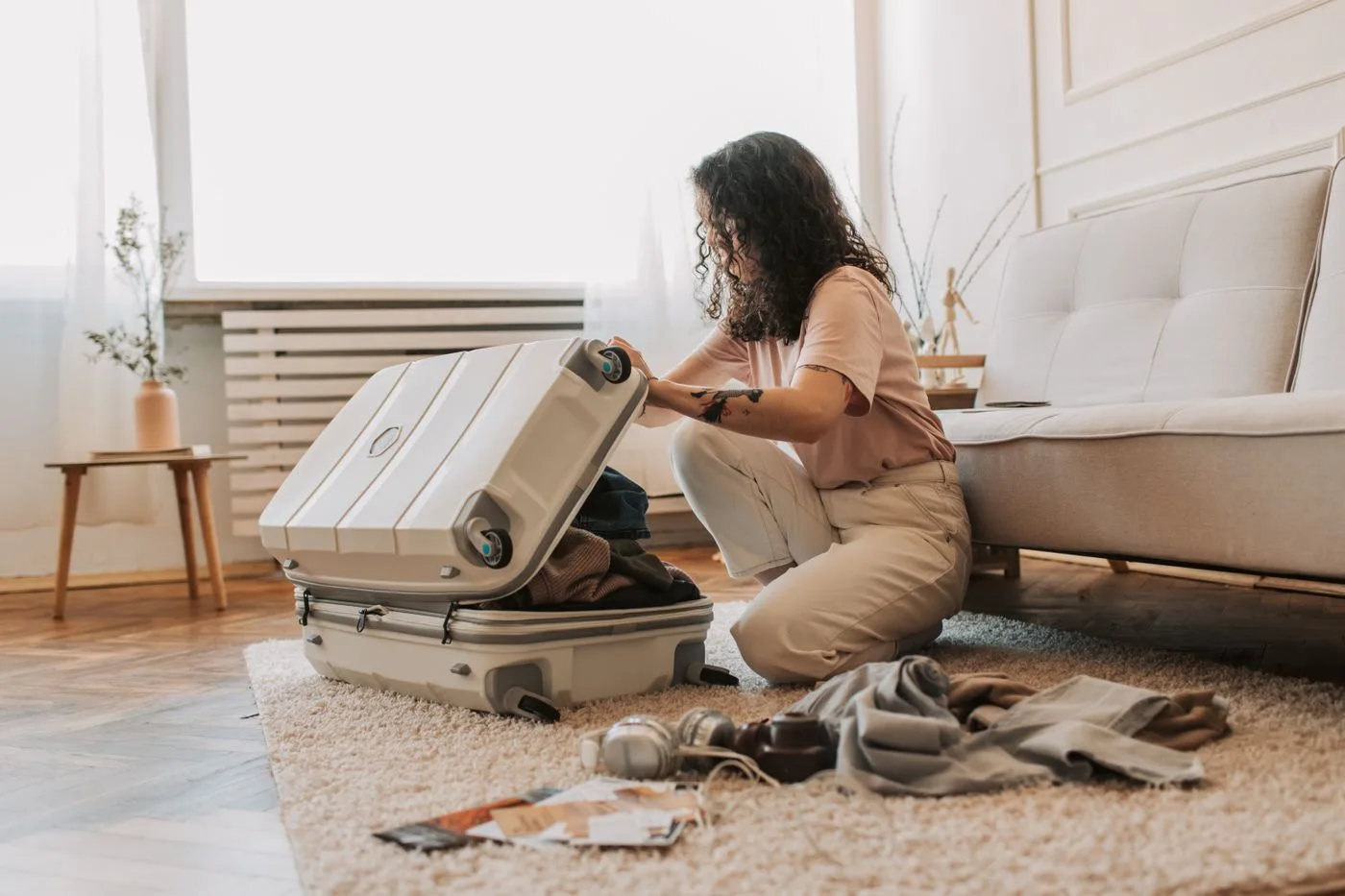 A woman packing an open hard-shell suitcase on the floor.
