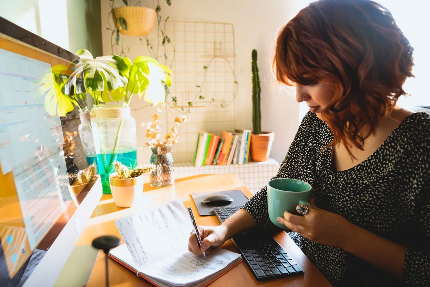 A woman writing in a notebook beside a green mug.