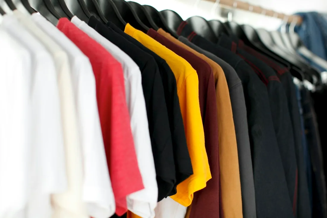 White, red, yellow, and dark tops hanging on a rail.